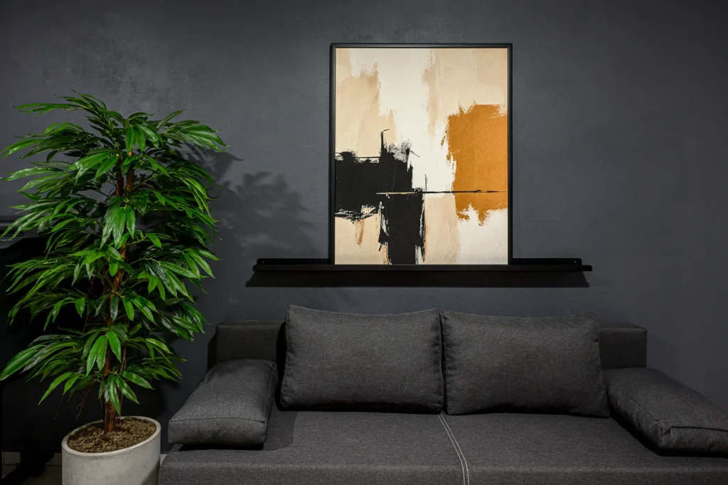 Zarámovaná fine art tlač na plátne 100 × 80 cm na výšku v čiernom drevenom ráme 22 mm, zavesená nad sivou pohovkou na tmavej stene
